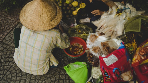 Vietnamesischer Markth&auml;ndler von Hinten mit Strohhut und vielen Marktprodukten um sich